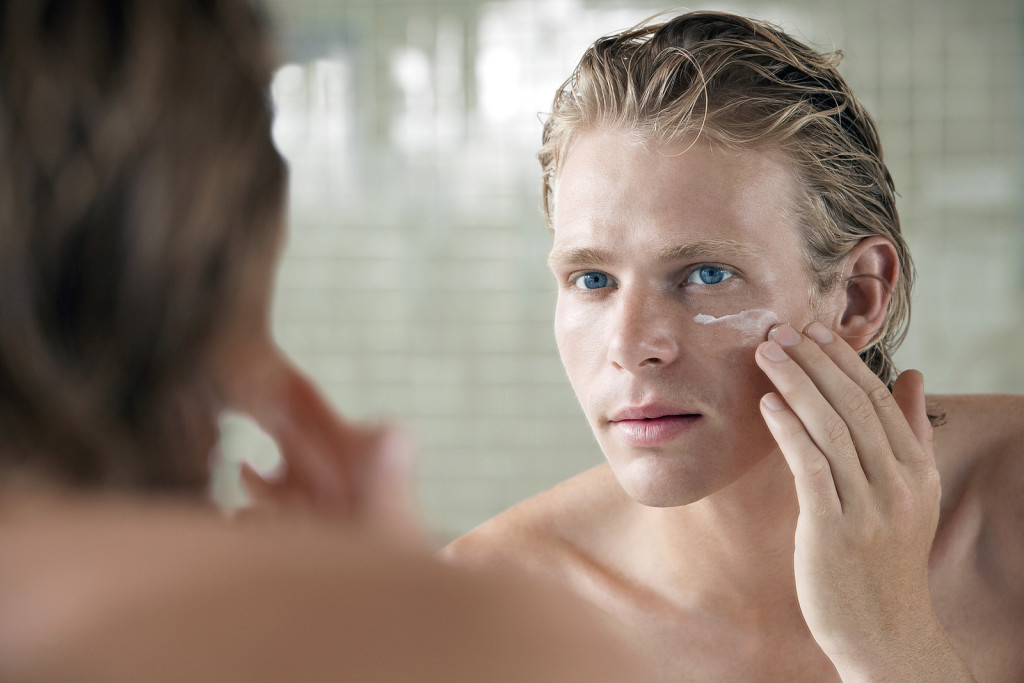 Closeup of handsome young man applying facial cream in front of