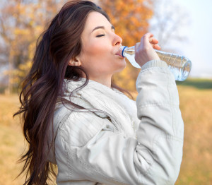 Young woman drinking water in the autumn park